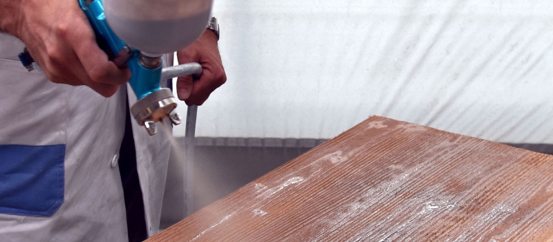Een persoon spuit met een machine beits over het hout in een donkere kleur