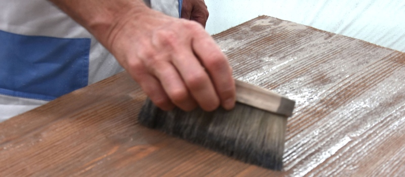 Een persoon brengt een grondlaag aan over het gebeitste hout en is dit aan het verdelen over het oppervlak