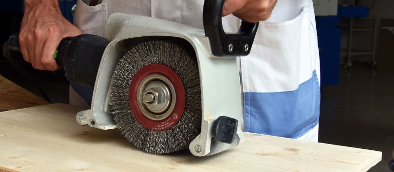 Iemand is bezig met een borstelmachine over hout te borstelen