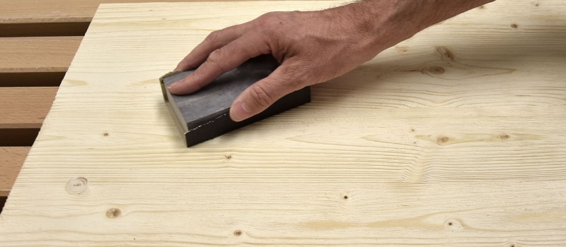 Een persoon is met met een schuurklosje in zijn handen het hout aan het schuren